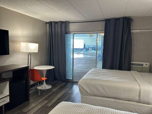A hotel room with two beds, a desk, a chair, a TV, and a view of the pool.