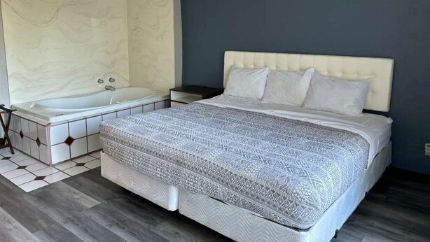 A bedroom with a large bed, a separate bathtub, and a nightstand.