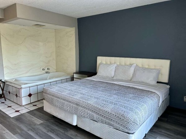 A bedroom with a large bed, a separate bathtub, and a nightstand.