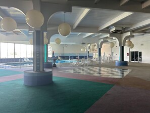 An indoor swimming pool area with multiple lanes, a checkered floor, and hanging spherical light fixtures.