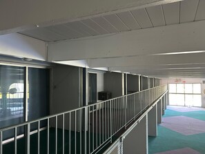 A multi-level indoor space with a metal railing, a green carpeted floor, and a window allowing natural light.