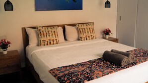 Ein Hotelzimmer mit einem Bett, einem Nachttisch mit Blumenvase und einem Wandbild eines Hais.