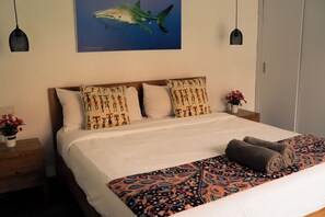 A hotel room with a bed, a nightstand with a vase of flowers, and a wall-mounted painting of a shark. - Cozy and Private 1BR Casa Su Villa in Seminyak (Badung)