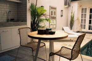 A kitchen with a round table and two wicker chairs, a small pool, and a lounge chair. - Cozy and Private 1BR Casa Su Villa in Seminyak (Badung)