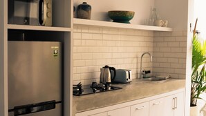 Eine moderne Küche mit Einbaukühlschrank, Mikrowelle und Herd. Es gibt ein Spülbecken mit Wasserhahn, einen Toaster und eine Schüssel auf einem Regal. Der Boden ist mit Fliesen ausgelegt, und es steht ein kleiner Mülleimer da.