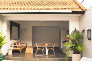 An open patio with a tiled roof, a wooden table, two chairs, a bench, and potted plants. - Cozy and Private 1BR Casa Su Villa in Seminyak (Badung)