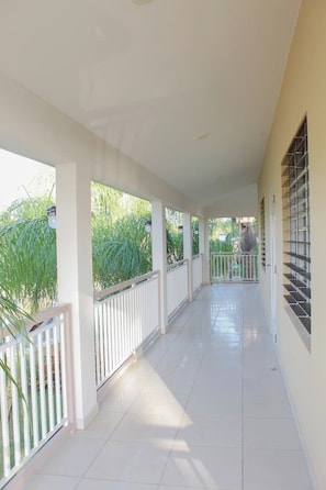 A covered corridor with white railings, a tiled floor, and a view of greenery outside. - Entire beachfront villa in Salinas, Puerto Rico (Salinas)