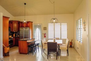A kitchen with wooden cabinets, a stainless steel refrigerator, and a dining area with a table and chairs. - Entire beachfront villa in Salinas, Puerto Rico (Salinas)