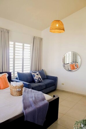 A bedroom with a bed, a sofa, a round mirror, and a hanging light fixture. - Entire beachfront villa in Salinas, Puerto Rico (Salinas)