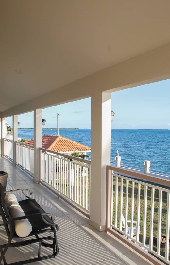 Un balcón techado con vistas al mar, una silla y una barandilla.