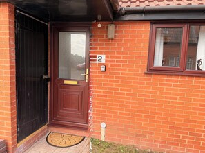 A red brick house with a black door, a window with a curtain, and a number '2' on the wall. - Hereford Stays — 2 Bed Bungalow, Sleeps 6, Parking, Wifi (Hereford)