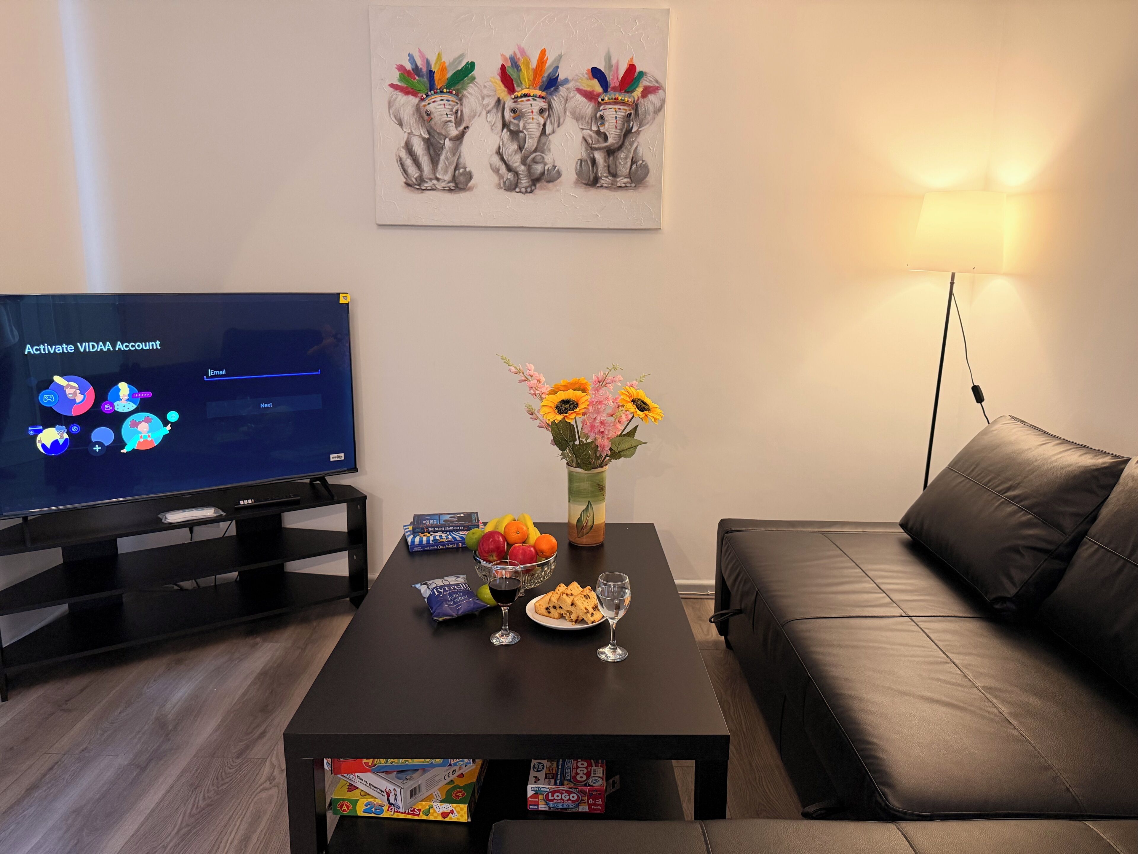 Ein Wohnzimmer mit Flachbildfernseher, Couch, Couchtisch mit Snacks und Getränken sowie einem Bild an der Wand.
