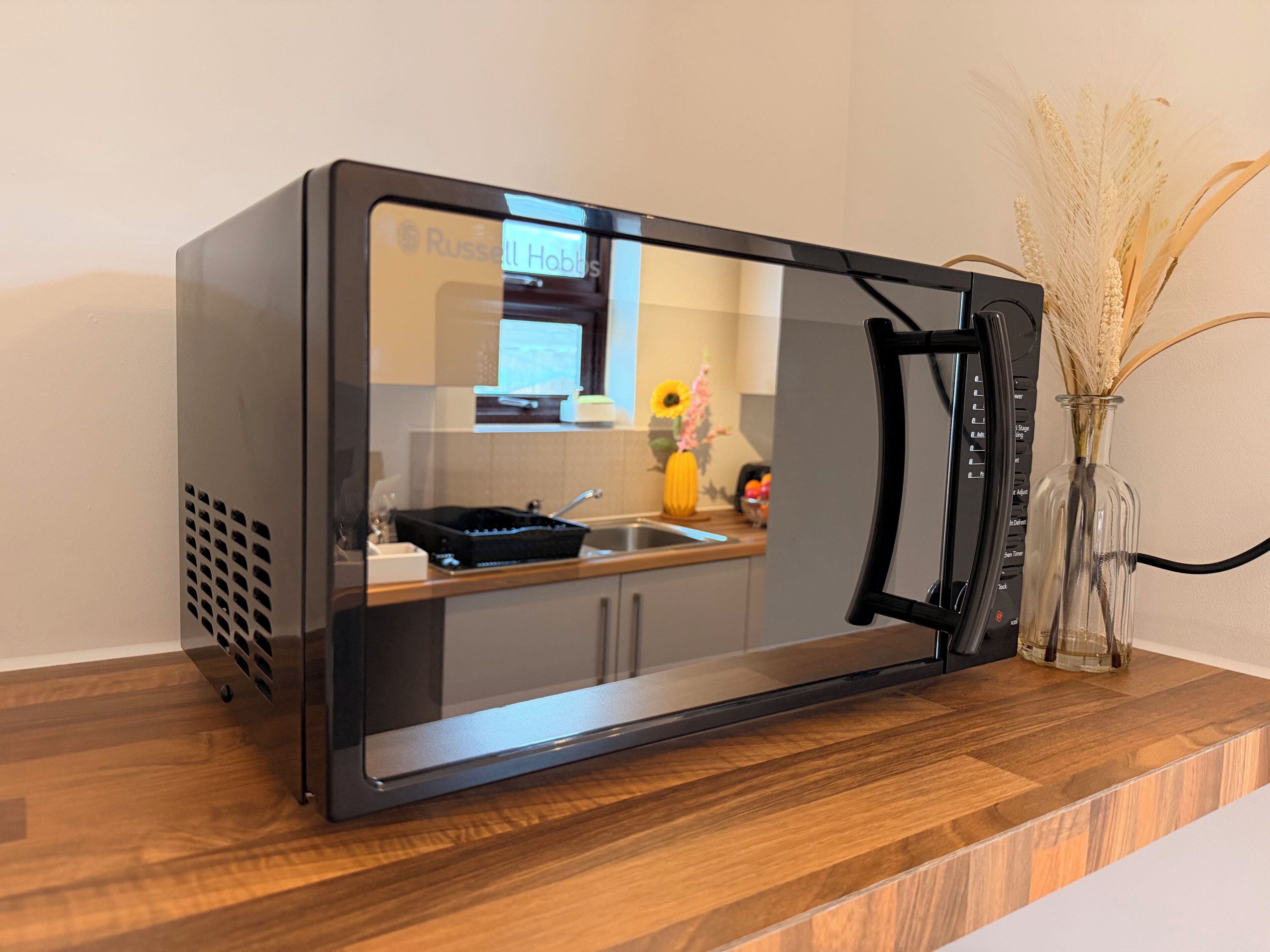 Una cocina moderna con microondas integrado, un lavamanos y un florero con plantas secas en la encimera.
