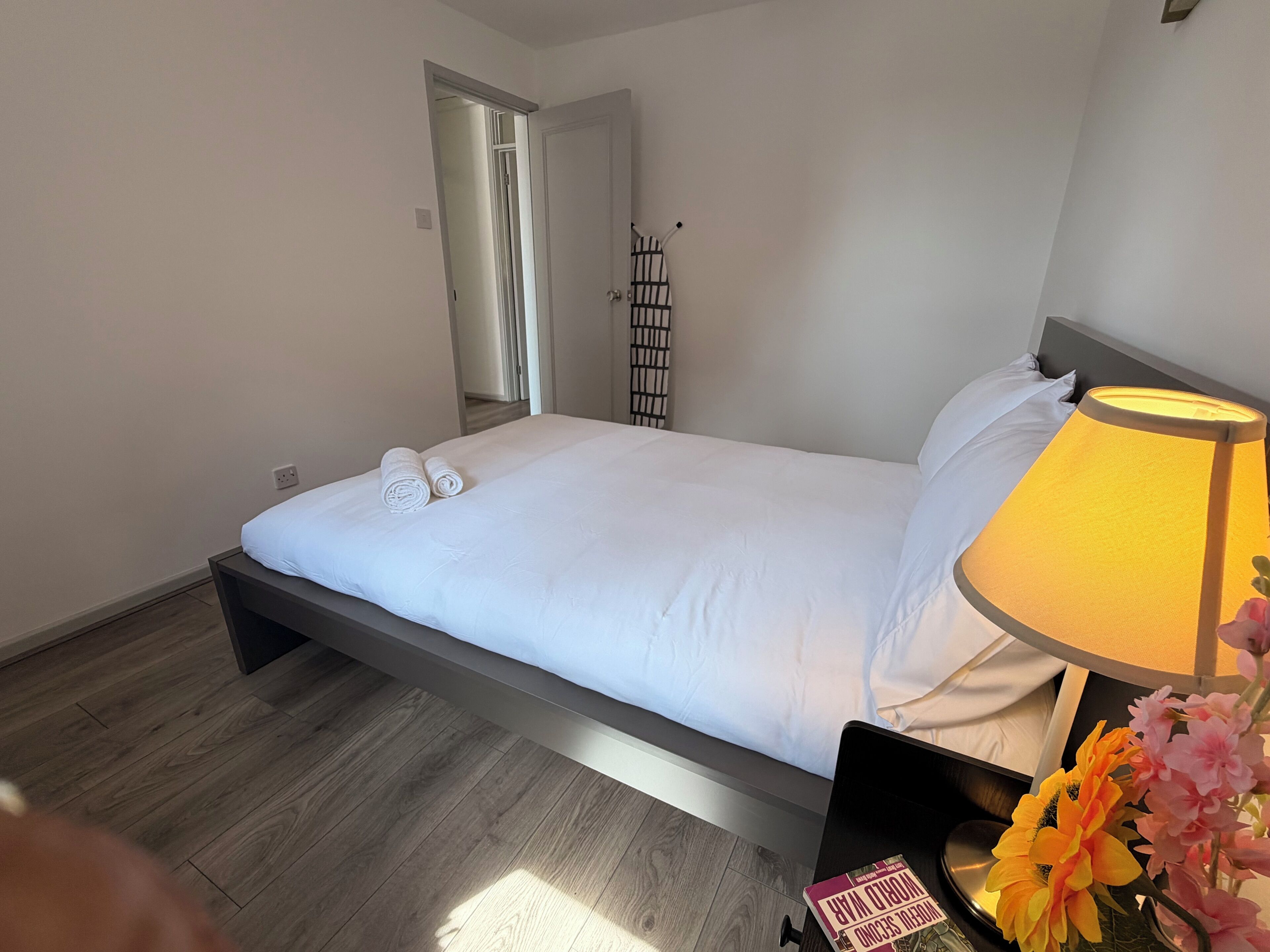 Una habitación de hotel con una cama, una lámpara de noche, una computadora portátil y un arreglo floral.