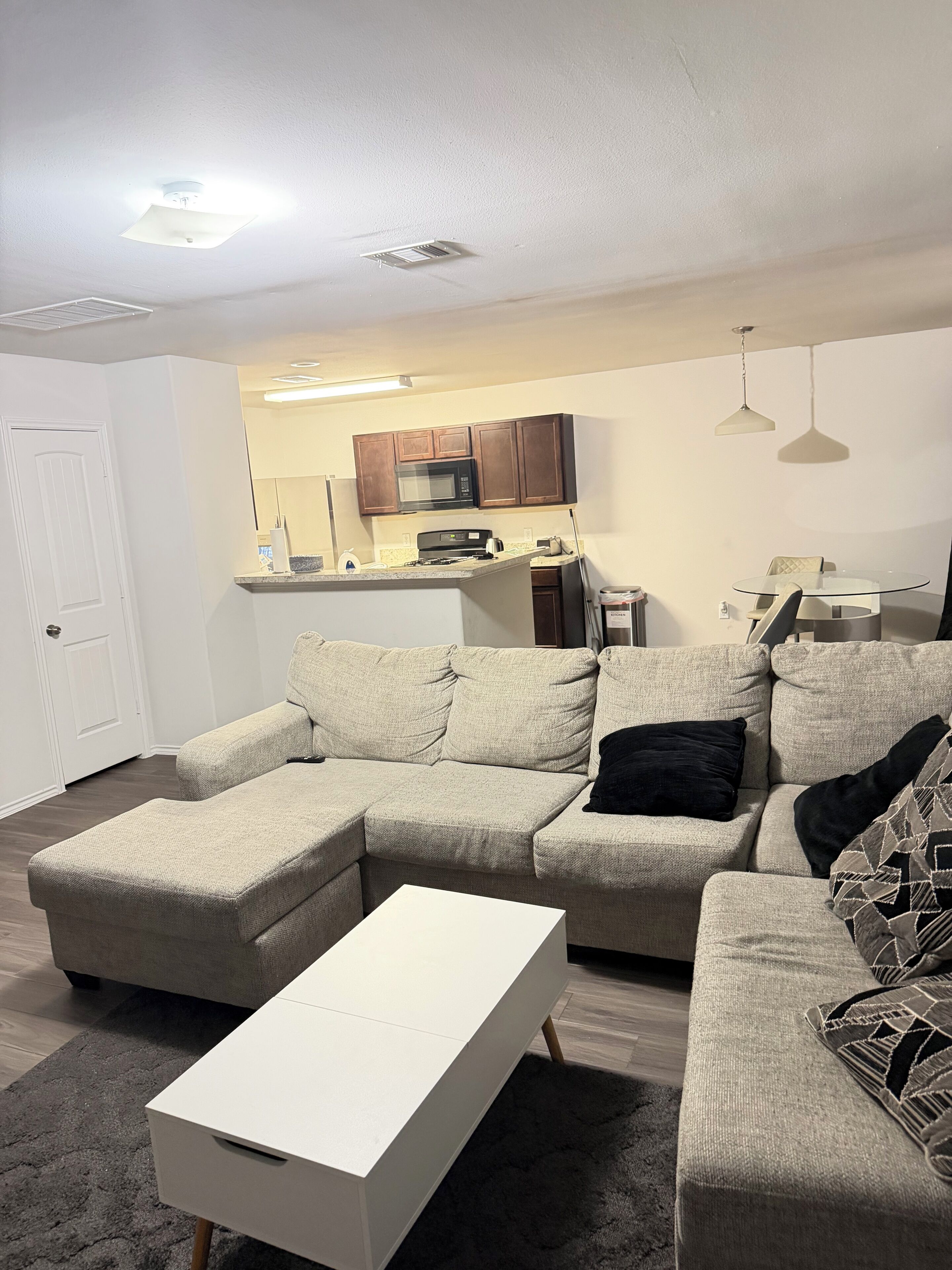 Una sala de estar con un sofá modular, una mesa de centro blanca y una cocina al fondo.