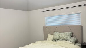 A bedroom with a bed, a bench, a window with blinds, and a ceiling light. -  A Peaceful Richmond Stay in Houston Made for Comfort & Memories. (Richmond)