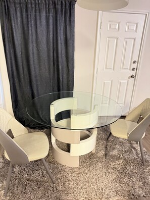 A round glass table with two chairs, a black curtain, and a white door in the background. -  A Peaceful Richmond Stay in Houston Made for Comfort & Memories. (Richmond)