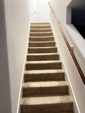 A carpeted staircase with a wooden handrail, leading to a white door at the top. -  A Peaceful Richmond Stay in Houston Made for Comfort & Memories. (Richmond)