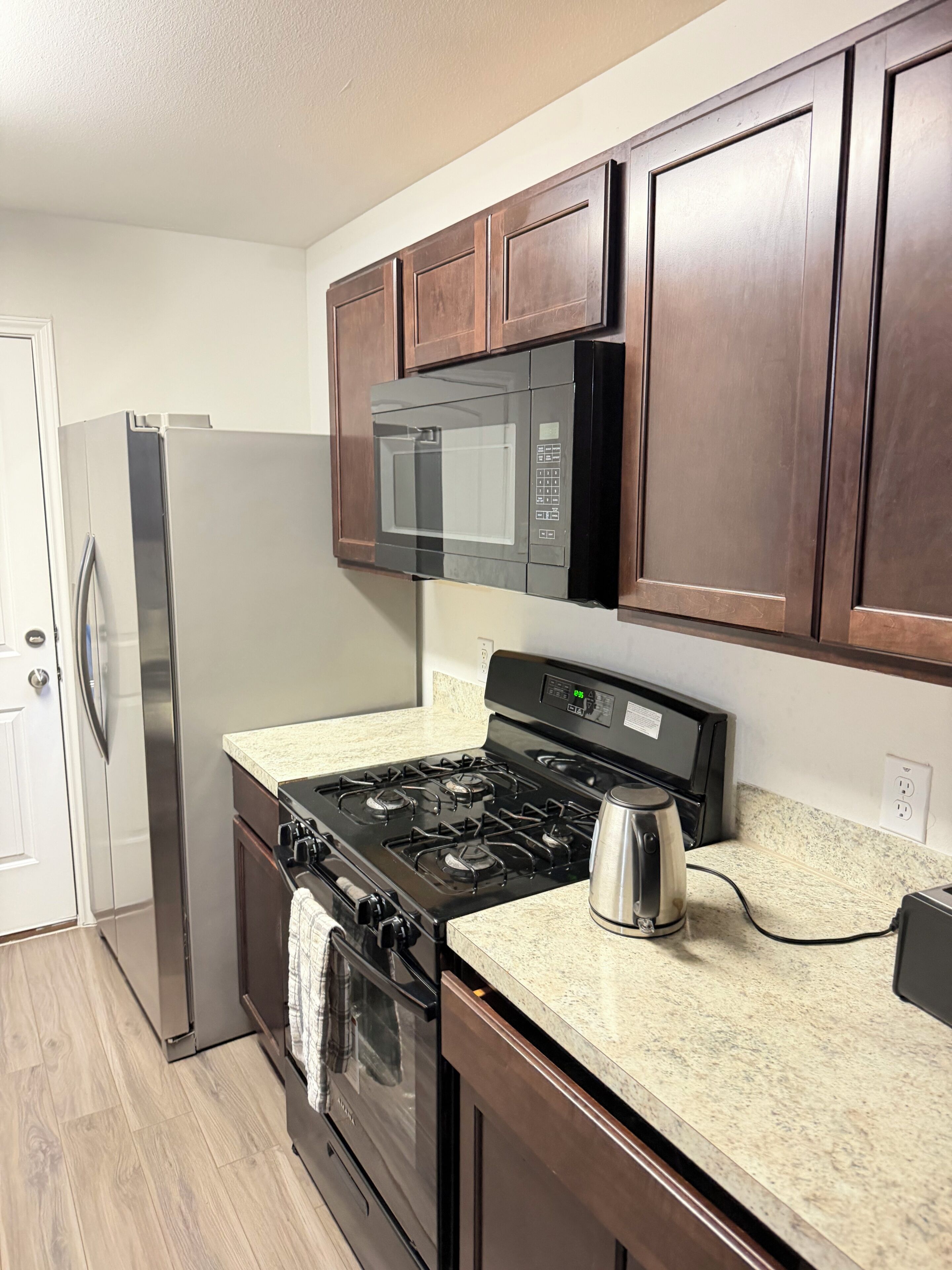 A kitchen with a stainless steel refrigerator, a microwave, a stove, and a coffee maker.