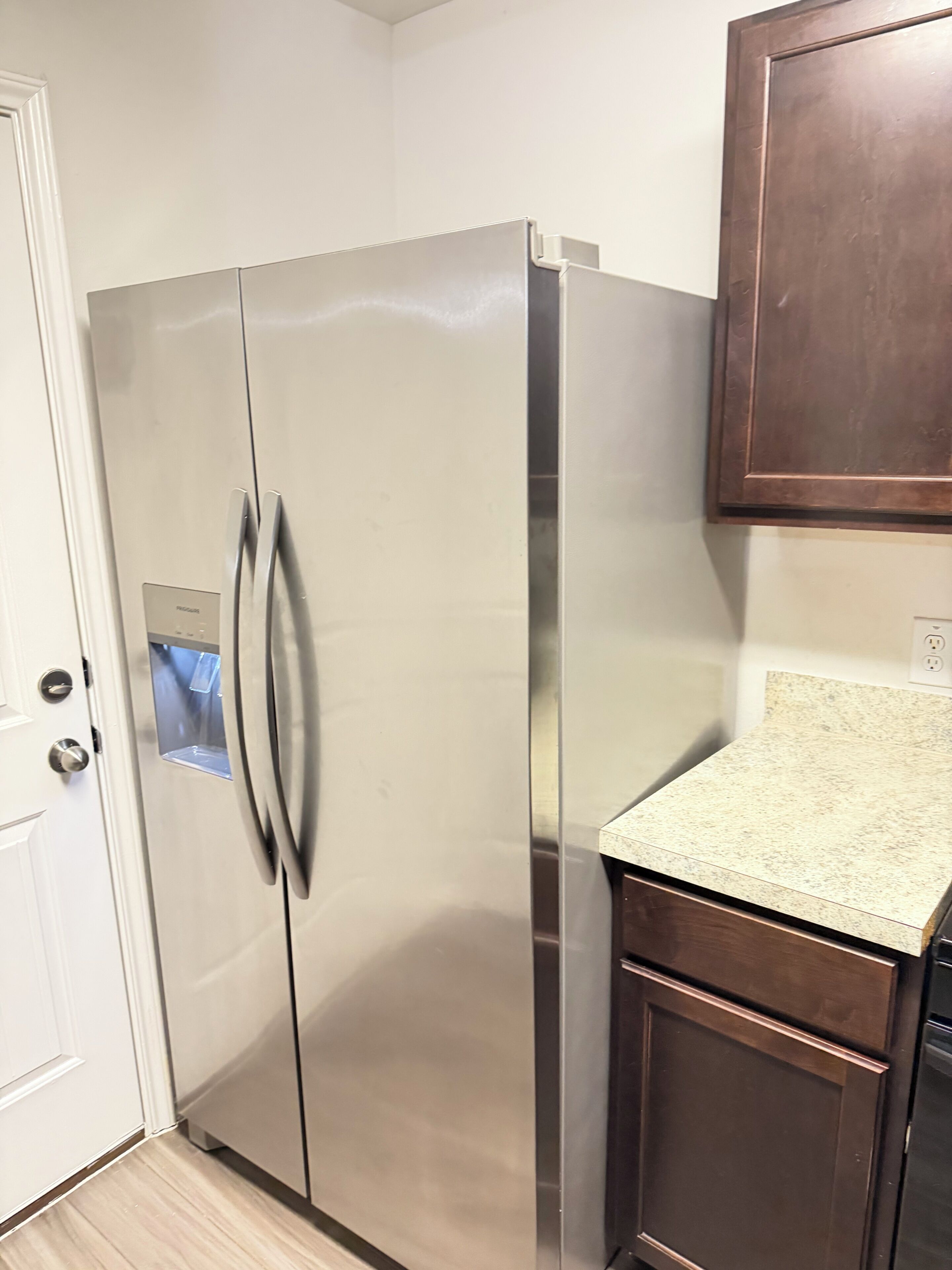 A stainless steel refrigerator with a freezer compartment, a wooden cabinet above it, and a granite countertop.