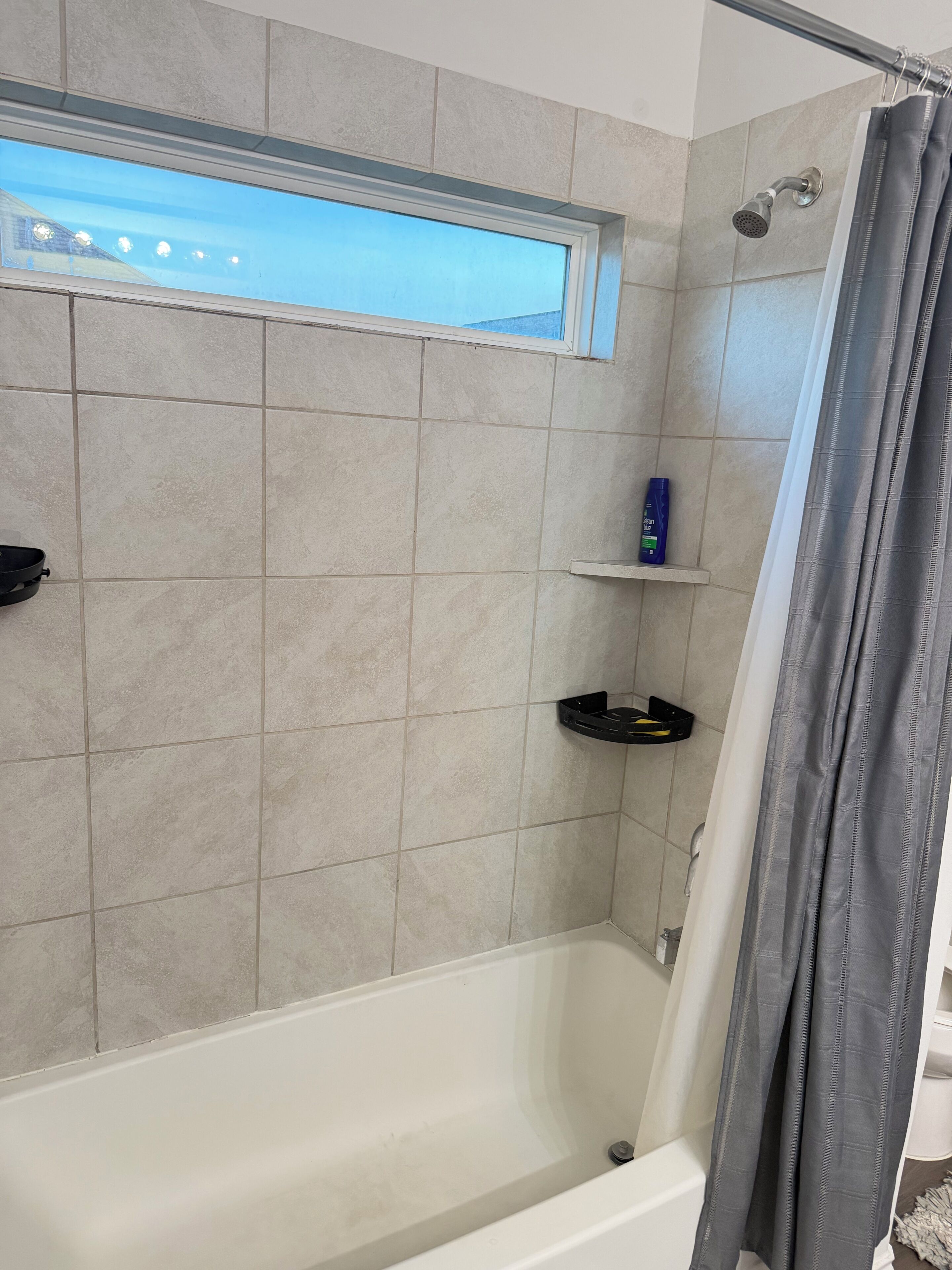 A bathroom with a bathtub, a shower curtain, and a shelf with toiletries.