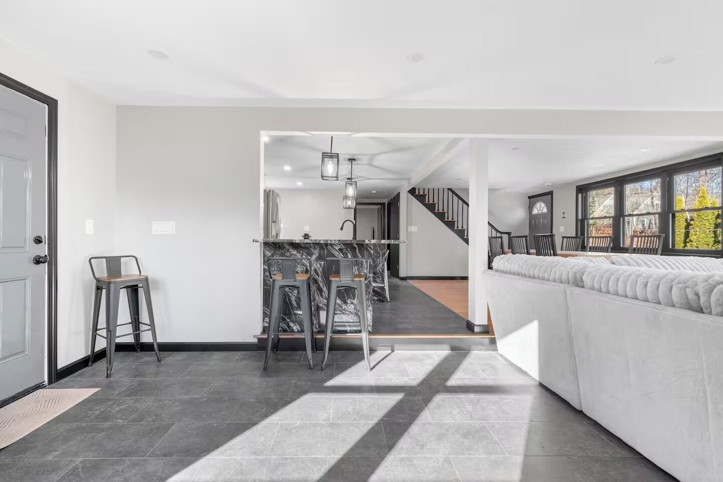 Ein modernes Interieur mit Küchenzeile, Barhocker, einer Couch und einer Treppe zu einer weiteren Ebene.