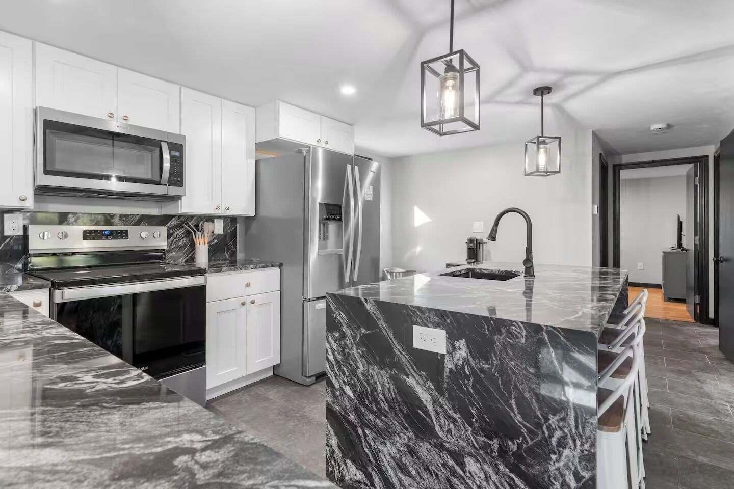 A modern kitchen with white cabinetry, a stainless steel refrigerator, a built-in oven, and a marble island with a sink.