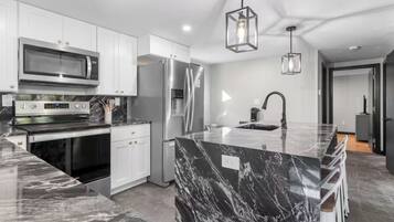 A modern kitchen with white cabinetry, a stainless steel refrigerator, a built-in oven, and a marble island with a sink.