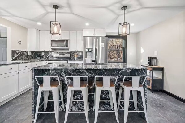A modern kitchen with a marble island, stainless steel appliances, and bar stools.