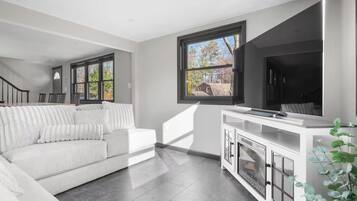 A modern living room with a white sofa, a flat-screen TV, and a large window with a view of the outside.