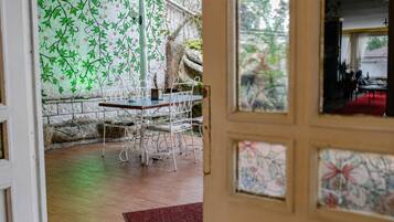 Une pièce comprenant un coin repas avec une table et des chaises, un mur en pierre orné d’un motif végétal, et une vue sur une autre pièce, accessible par une porte.
