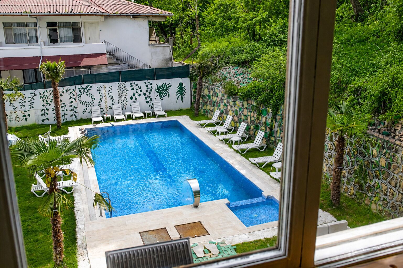 Une piscine rectangulaire avec une terrasse carrelée, entourée de chaises longues blanches et de palmiers.