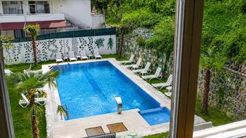 Une piscine rectangulaire avec une terrasse carrelée, entourée de chaises longues blanches et de palmiers.