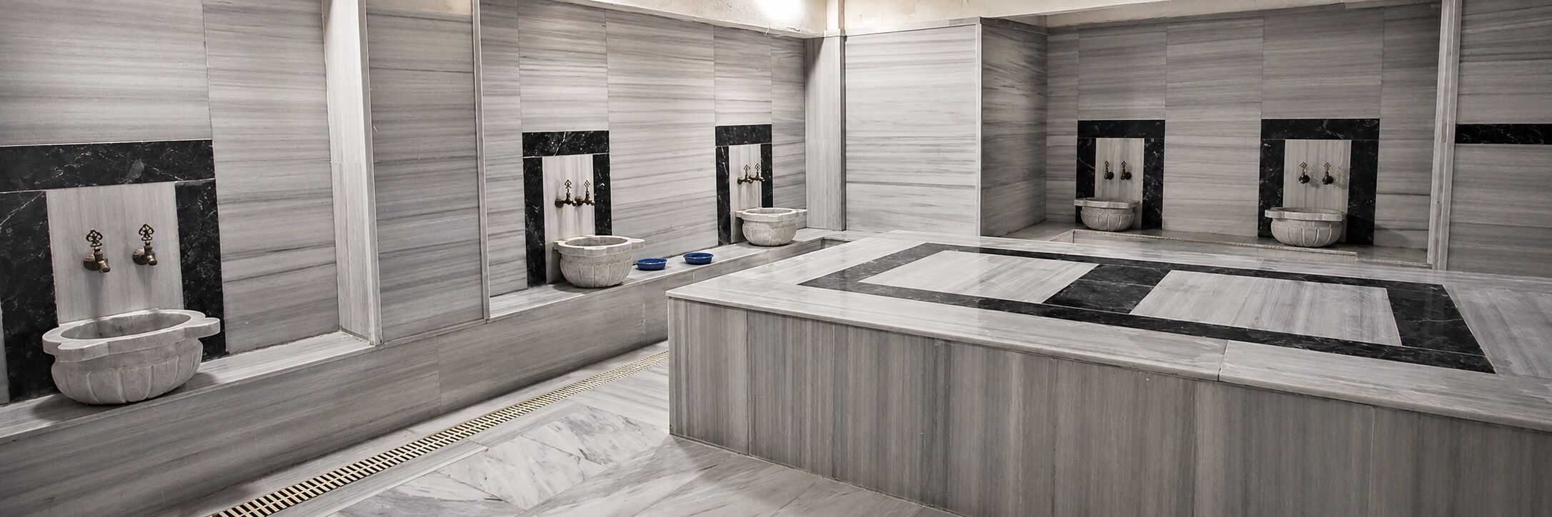 A modern bathroom with a central sink, multiple toilets, and a large mirror.