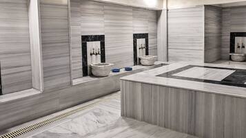 A modern bathroom with a central sink, multiple toilets, and a large mirror.