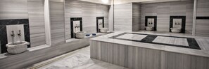 Un baño moderno con un lavamanos central, varios inodoros y un espejo grande.