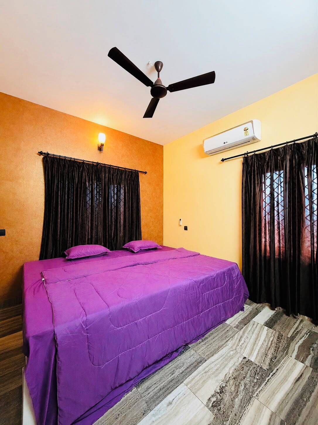 Una habitació amb llit, ventilador de sostre, aire condicionat i finestra amb cortines.