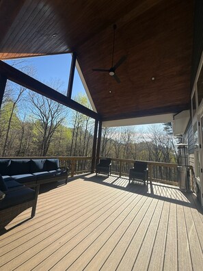 Une terrasse couverte avec un ventilateur de plafond, des sièges d’extérieur et une vue sur les arbres.