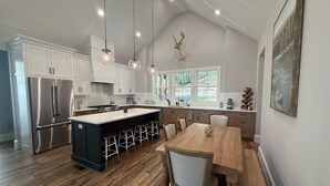 Una cocina moderna con una isla central, electrodomésticos de acero inoxidable y un comedor con mobiliario de madera.
