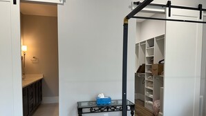 Un dormitorio con cama, una mesita de noche con caja de pañuelos, un armario con repisas y un baño con lavamanos y espejo.