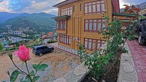 A two-story building with a traditional architectural style, featuring a balcony and a view of a mountainous landscape.