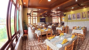 A dining area with multiple tables and chairs, wooden ceiling beams, and large windows.