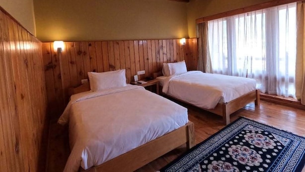A room with two wooden beds, a patterned rug, and a window with curtains.