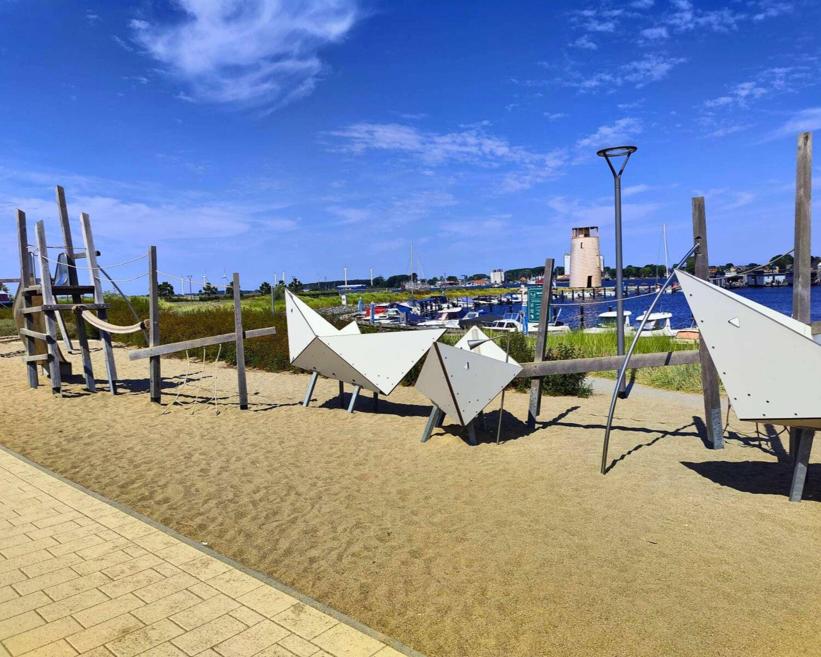 Una spiaggia con una passeggiata sabbiosa, un faro e barche sullo sfondo.