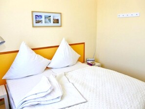 A hotel room with a bed, pillows, a bedside table with a lamp, and a wall-mounted picture. - Apartment am Sudstrand in Fehmarn-burgtiefe (Fehmarn)