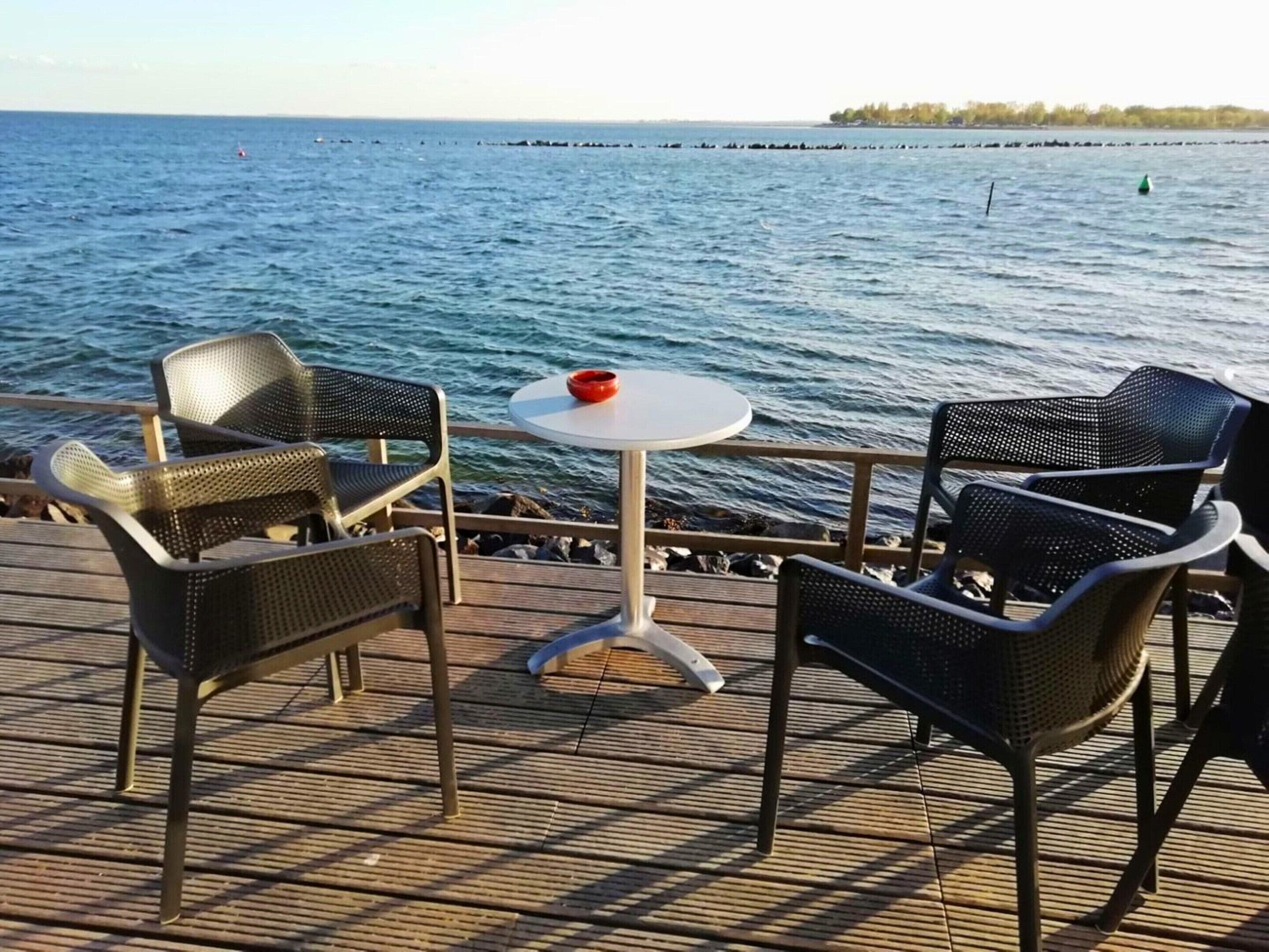 Une terrasse dotée de deux fauteuils en osier et d’une petite table ronde, offrant une vue sur une mer calme et une côte lointaine.