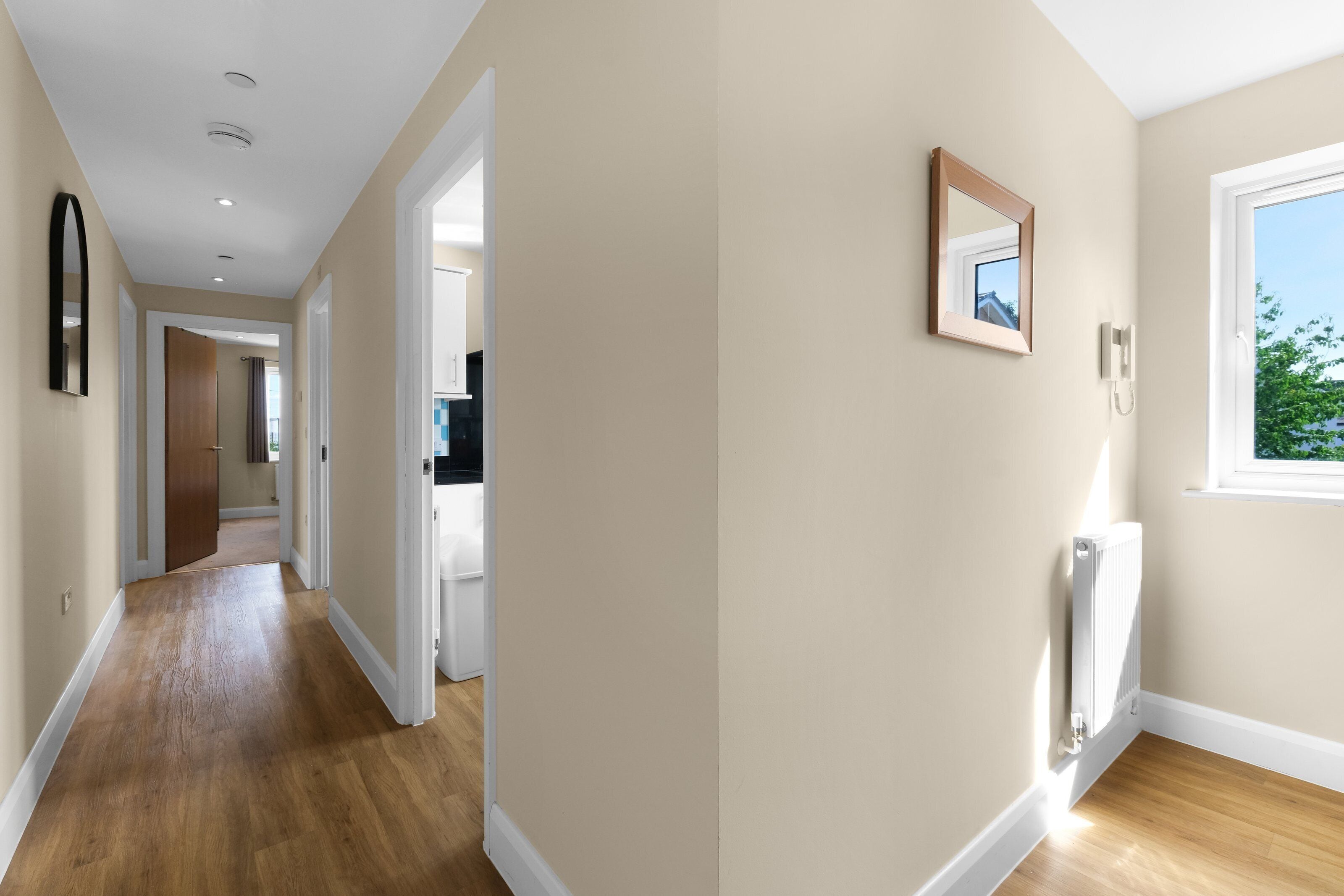 A hallway with wooden flooring, a white door, and a window with a view of greenery.