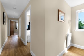 A hallway with wooden flooring, a white door, and a window with a view of greenery. - Heathrow Living Apt. 08 by 360 Stays (Stanwell)