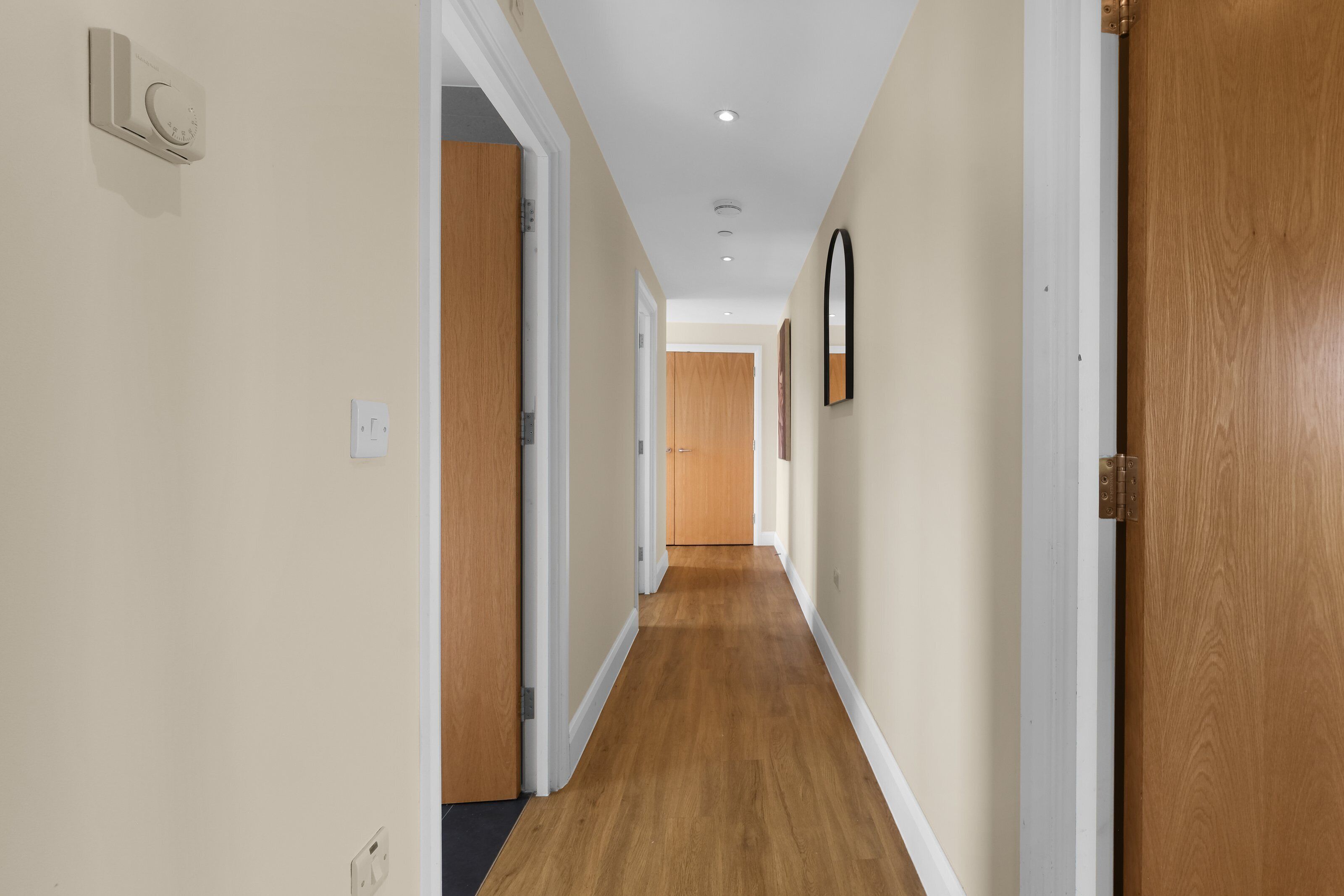 A hallway with wooden flooring, white walls, and doors on both sides.