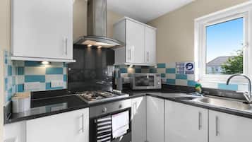 A modern kitchen with white cabinets, a gas stove, a microwave, and a window with a view.